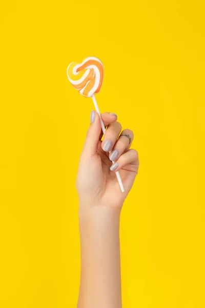 Mooie geprepareerde vrouwen hand met het houden van snoep op gele achtergrond — Stockfoto
