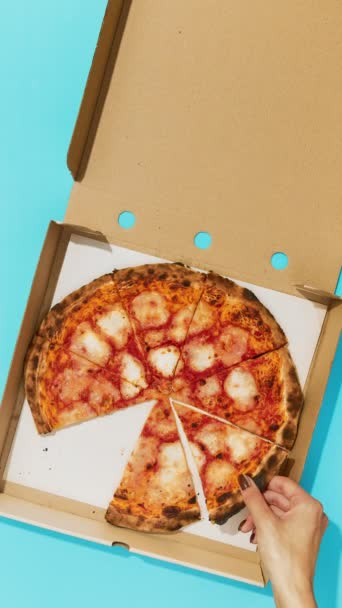 Flat lay bovenaanzicht handen nemen van pizza snijdt uit doos op blauwe tafel — Stockvideo