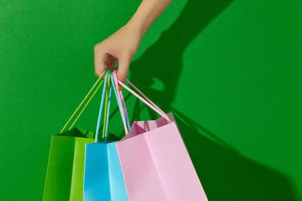 Ženská ruka drží nákupní tašky na zeleném pozadí. Koncept nákupního prodeje — Stock fotografie