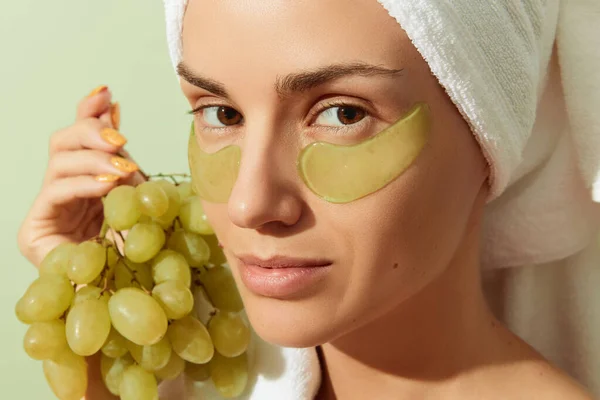 Femme utilisant des patchs pour les yeux à base de pépins de raisin sur fond vert pastel. Soins naturels durables pour la peau — Photo