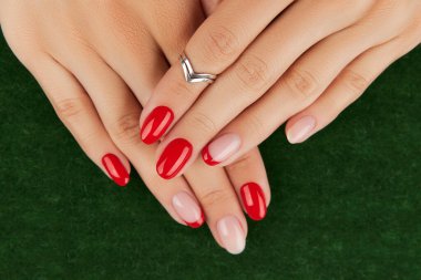 Yeşil arka planda kırmızı modern manikürlü kadın elleri. Manikür tasarım eğilimleri.