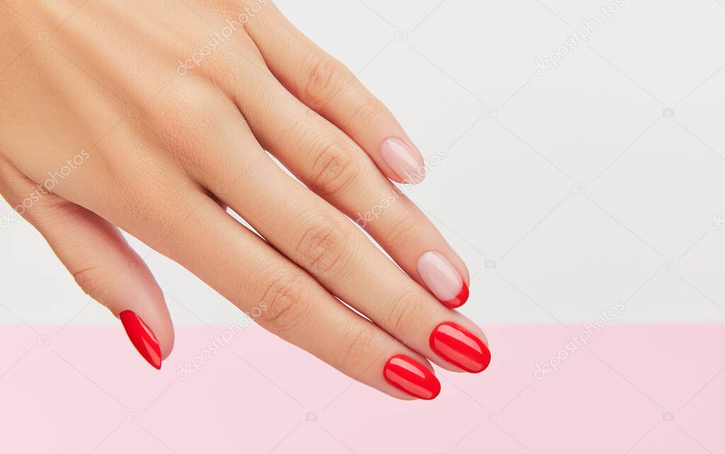 Womans hand with fashionable red manicure over white and pink background