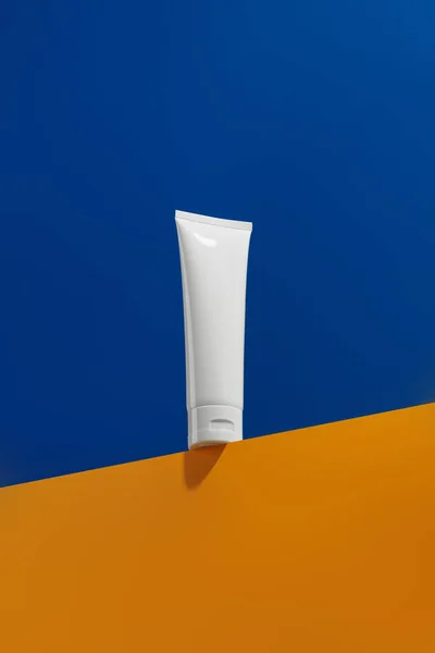 Mavi ve turuncu yaratıcı arka planda cilt bakım ürünü içeren boş beyaz tüp.