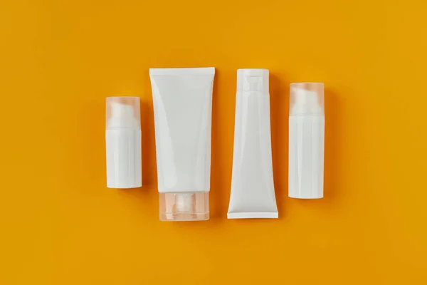 Επίπεδη lay top view λευκά μπουκάλια σωλήνες με προϊόντα φροντίδας του δέρματος σε πορτοκαλί δημιουργικό υπόβαθρο — Φωτογραφία Αρχείου