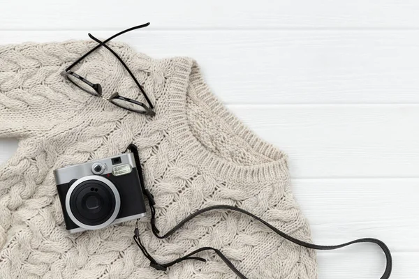 เสื้อกันหนาวฤดูใบไม้ร่วงของผู้หญิงและกล้องทันทีบนพื้นหลังไม้สีขาว — ภาพถ่ายสต็อก