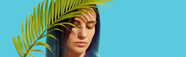 Young beautiful woman with blue hair holding palm leaf on bright background — 스톡 사진