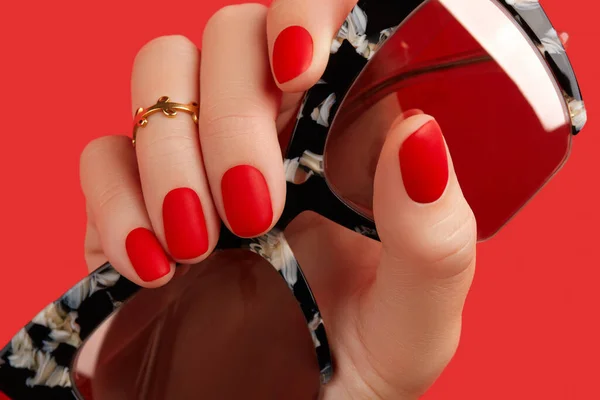 Womans hand holding sunglasses over red background. Manicure, pedicure design trends — Stock Photo, Image