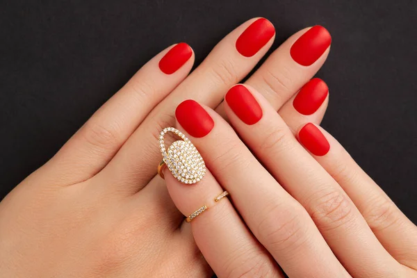 Zamknij kobietom ręce z czerwonymi matowymi paznokciami na czarnym tle. Manicure, pedicure trendy projektowe — Zdjęcie stockowe