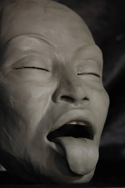 face with facial expression and tongue, in clay on black background