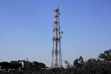 Kırsal kesimin siyah-beyaz görüntüsü. Mavi gökyüzü ve renkli haberleşme kulesi. Kablosuz iletişim için anten vericisi: 3G, 4G, 5G