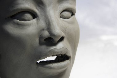 Asyalı kadın yüzü. Islak kil heykel. Doğulu gözler, burun, dişler ve ağız ayrıntıları. Beyaz arkaplandaki heykelin ayrıntıları