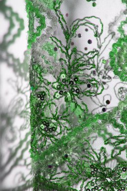 Şeffaf perdenin gölgesi ve duvardaki çiçek desenleri. Karmaşık nakış işleriyle süslenmiş yeşil kumaş. Tel, pullar ve boncuklar..