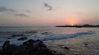 Uçurumdan gün batımının olduğu güzel bir liman manzarası. Kayalarda yavaş çekim dalgaları.
