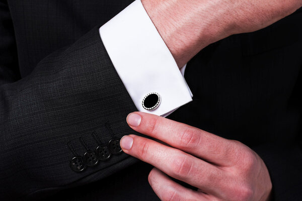 elegant young fashion man looking at his cufflinks while fixing them