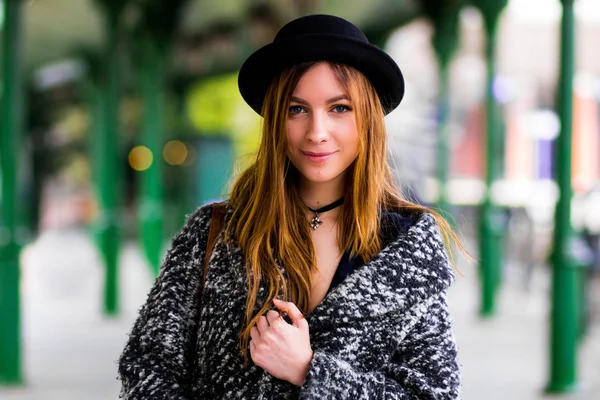 Young beautiful girl in a hat and a short dress and jacket on a background of green poles — Stock Photo, Image