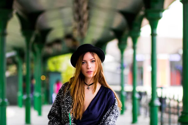 Young beautiful girl in a hat and a short dress and jacket on a background of green poles — Stock Photo, Image