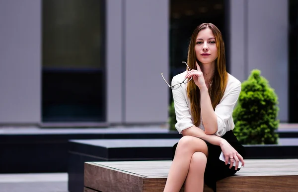 Schöne schlanke Mädchen sexy auf dem Hintergrund der strengen Gebäude im Stil des Büros hält eine Brille. Porträt — Stockfoto