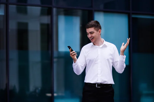 Portrait of a young successful businesslike man with a cell phone conversation while standing near the office of the interior male professional banker in a suit holding a cell phone concept background
