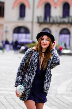 Genç, güzel bir kız, elinde çanta ve bir fincan kahveyle sokakta yürüyor..