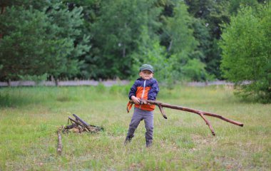 Elinde sopayla ormanda oynayan 4 yaşında bir çocuk.
