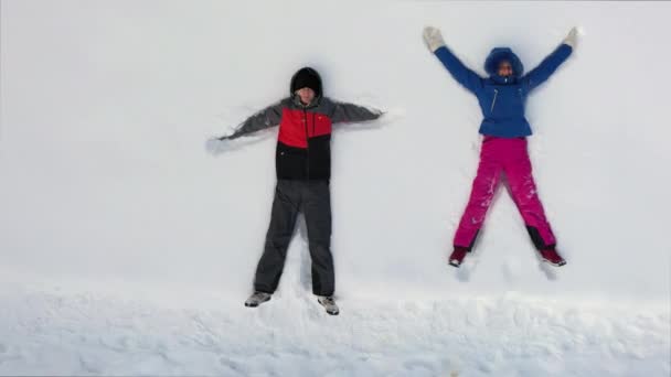 晴れた冬の日には幸せな白人女性と男性の空中トップビュー 雪の中に飛び込んで雪の天使をして — ストック動画