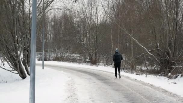 冬のスポーツとレクリエーションの概念 冬の都市公園の雪道をジョギングする無名の男 — ストック動画
