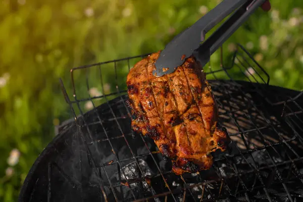味付けされた豚肉を持つグリルトングの写真を閉じます バーベキューグリルの外で肉を焼く 夏の屋外グリルパーティー 健康的なバーベキュー — ストック写真