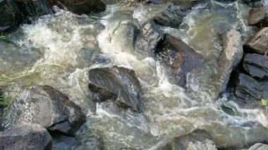Nehirden taşların üzerinden bir gölete akan hızlı suyun yakın görüntüsü..