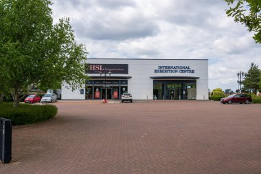 Norwich, UK- 17 Mayıs 2025: Modern sergi merkezi ve Norwich, Norfolk 'ta tuğla döşeme ve park yeri ile perakende satış mağazası. Ağaçları ve bulutlu gökyüzü olan beyaz ticari bina.