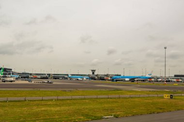 Amsterdam, Hollanda... 24 Mayıs 2025: AMS havaalanında birden fazla uçak, pistteki KLM filosu da dahil. Schiphol Havaalanı panoraması bulutlu bir günde kapılar, pist ve terminal tesislerinde uçakları gösteriyor.