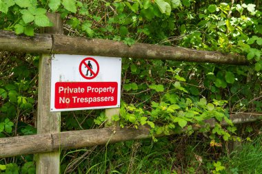 Yeşil yapraklı eski ahşap bir çitte kırmızı ve beyaz özel mülk tabelası var. Etrafı yemyeşil bitkiler ve tırmanan sarmaşıklarla çevrili kırsal çitlere izinsiz giriş uyarısı asılmadı.. 