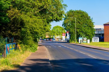 Norwich, UK- 17 Mayıs 2025: Asfalt yolu, çim kenarları, sokak lambaları ve sakin bir yaz akşamında açık mavi gökyüzünün altındaki yerleşim alanından geçen tabela