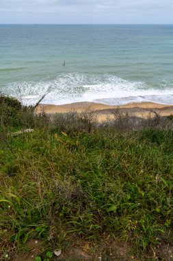 Cromer, İngiltere 'deki çimenli kayalıklardan beyaz dalgalar ve okyanus manzaralı kumlu sahil manzarası, sakin mavi deniz suyu üzerinde bitki örtüsü ve ufuk ile huzurlu deniz manzarası