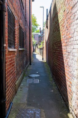 Norwich, UK- 17 Mayıs 2025: Eski şehir merkezindeki tuğla binalar arasındaki atmosferik dar geçit. Eski kırmızı tuğla cepheleri ve mesafeye uzanan beton kaldırımları olan İngiliz kentsel sokakları.