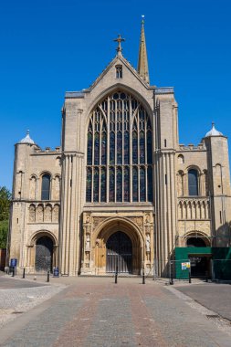 Norwich, UK- 17 Mayıs 2025: Muhteşem Gotik katedral cephesi yüksek sivri uçlu kemerler ve açık mavi gökyüzünün altındaki vitray pencereler. Süslü taş girişli tarihi ortaçağ kilise mimarisi.
