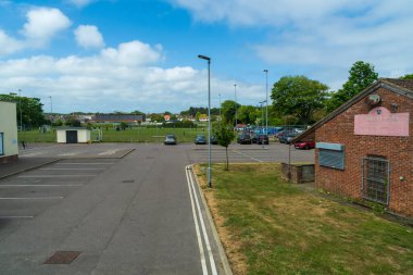 Cromer, UK- 18 Mayıs 2025: Asfalt park alanı olan yerel spor sahası, tuğla pavyon binası, çim sahaları, lamba direkleri, ağaçlar ve arka plandaki evler