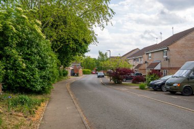 Norwich, UK- 17 Mayıs 2025: tuğladan evleri, park edilmiş arabaları ve olgun ağaçları olan yapraklı banliyö caddesi. Çevresi yemyeşil yeşillik ve bahçe bitkileriyle çevrili sessiz bir mahalle.