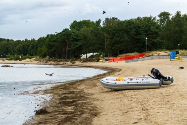 Tallinn, Estonya - 21 Ağustos 2025: şişme motorlu tekne kumlu sahil şeridinde dinleniyor orman arka planında ve kuşlar uçuşuyor. Cankurtaran kurtarma ekipmanlarıyla sessiz Baltık sahnesi
