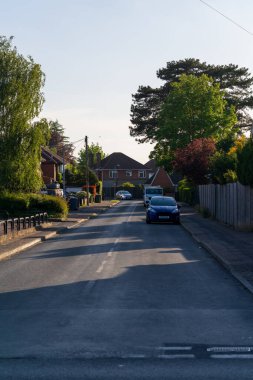 Norwich, UK- 17 Mayıs 2025: Tipik bir banliyöde akşam ışığı altında evler, araçlar ve yemyeşil yapraklarla kaplı sakin bir yerleşim yeri.