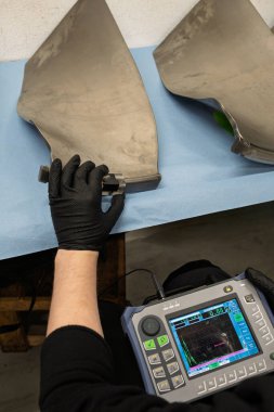 Uçak türbini pervanelerinin taşınabilir test cihazıyla ultrasonik kontrollerini yapan teknisyen, havacılık bakımı sırasında dijital ekranda tarama sonuçlarını gösteriyor.