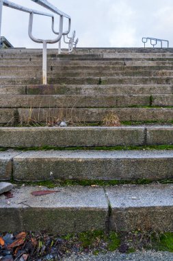 Terk edilmiş beton merdivenler, yıpranmış metal korkuluklar kentsel bozulma, yosun ve bitki örtüsü büyümesi, bozulma ve bulutlu gökyüzü koşulları altında ihmal belirtileri gösteriyor.