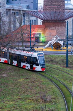 Tallinn, Estonya - 20 Aralık 2025: Şehir ortamında raylar üzerindeki modern elektrik tramvayı. Şehrin arka planında tarihi tuğla binalar bulunan bir bölgesinde toplu taşıma aracı hareket ediyor.
