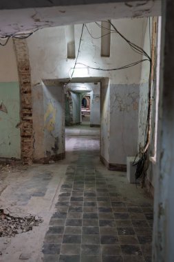 Hapishane iç koridoru yıkık duvarlar, tuğlalar ve fayanslarla döşenmiş döşemeler, eski terk edilmiş hapishane koridoru elektrik kabloları ve hasar görmüş tavan yapısı ile kentsel çürümeyi gösteriyor.