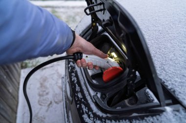Kış Karları 'nda Otomobil Limanı' na elektrik kablosu bağlayan kişi. EV Sahibi Soğuk Hava Mevsiminde Şarj Etmek için Otomobile Bağlanıyor