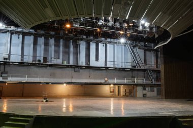 Profesyonel ışıklandırma ekipmanlarıyla terk edilmiş belediye salonunun boş sahnesi. Terk edilmiş belediye tiyatrosu ahşap zemin, balkon oturma seviyeleri ve teknik donanım altyapısını gösteriyor.