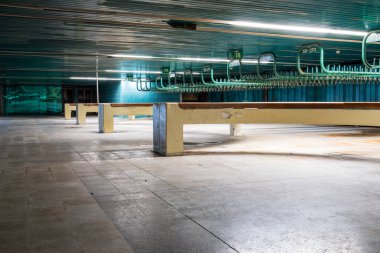 İçinde yeşil seramik duvarlar ve numaralı palto kancaları olan terk edilmiş bir vestiyer. Belediye kostüm odasında beton çıkıntı, uzun askılık ve hareket bulanıklığı var.