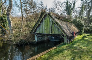Run down thatched boathouse on Norfolk Broads surrounded by tree clipart