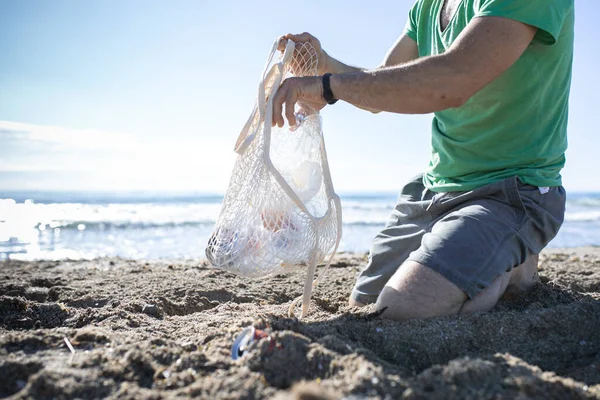 Man hand picked plastic bottle waste on beach. mesh bag. Man cleaning the beach from plastic.Selective focus