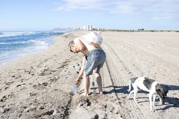 Man and his dog cleaning the beach of plastic bottles. Selective focus. Copy space