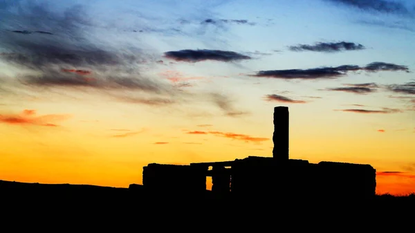 Silhouette of old ruined abandoned house with large chimney in front of colorful sunset, Iceland